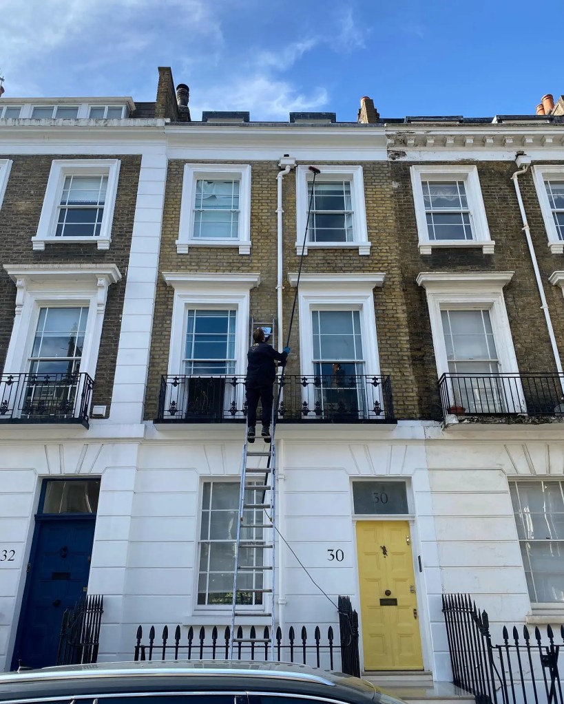 Diamond Gutters UK Cleaning windows on a three-story building using an extendable pole, reaching high floors with precision and care