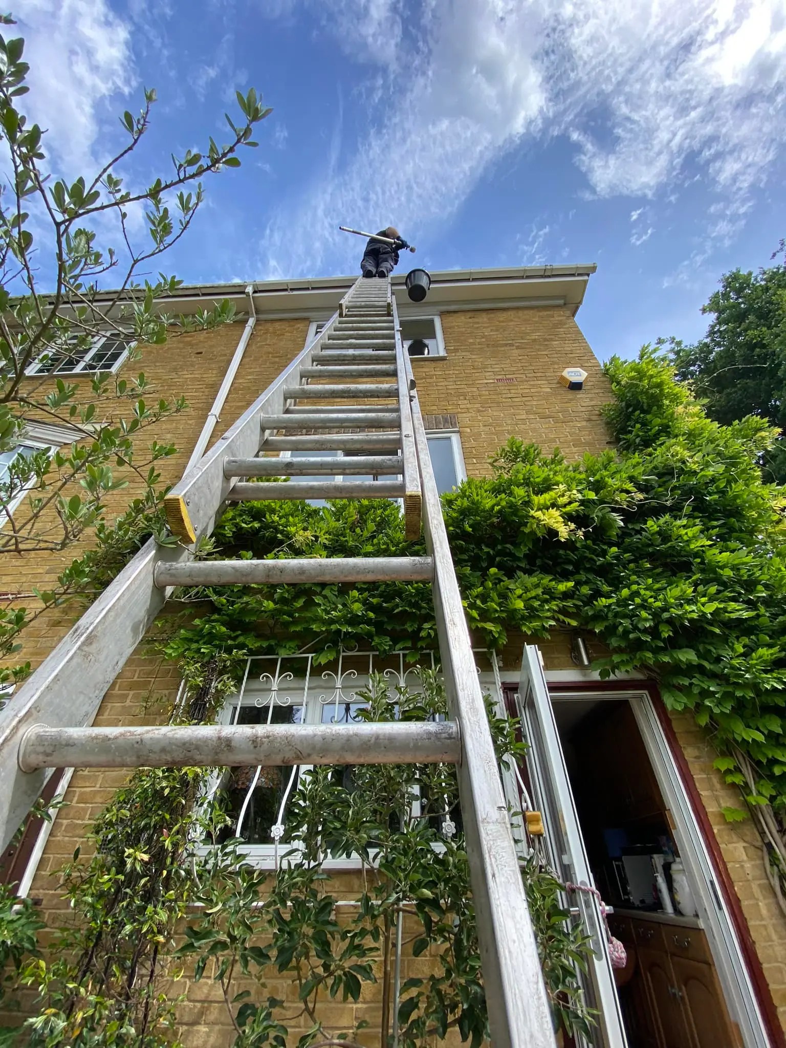 Diamond Gutters UK employee climbing a three-story building to clean the roof, showcasing professionalism and commitment to high-quality service