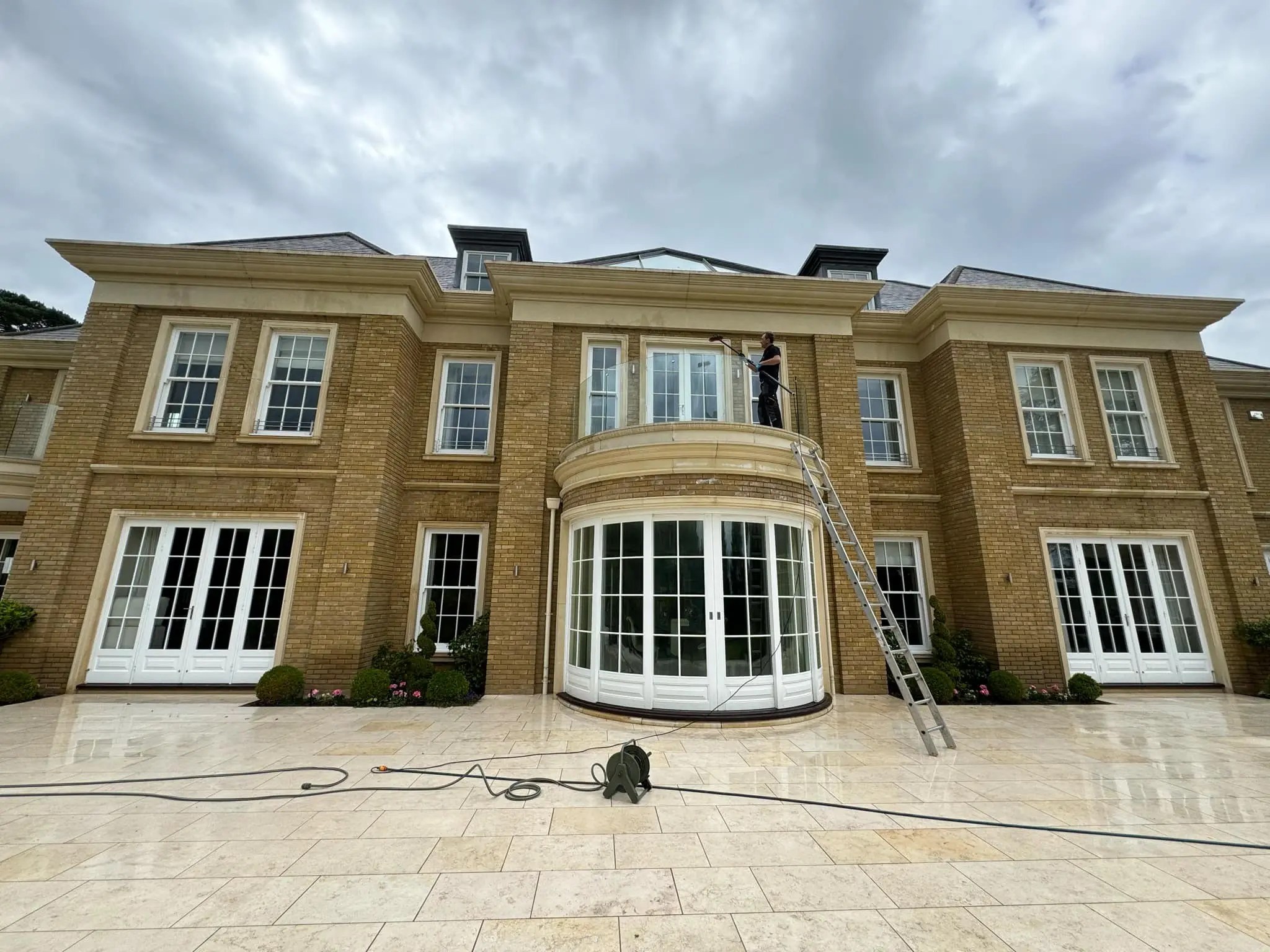 Diamond Gutters UK employee climbing above the front door to clean second-floor windows