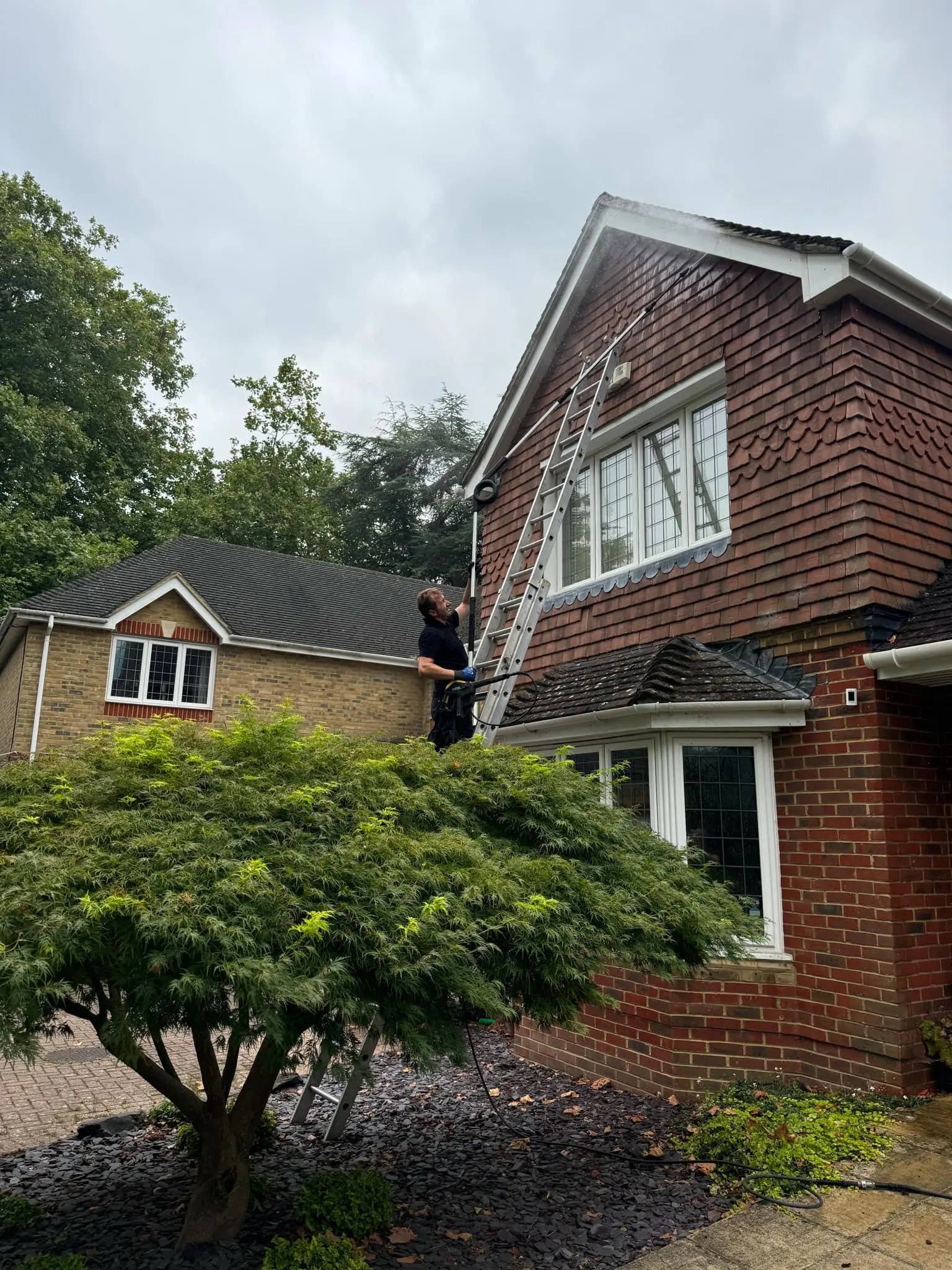 Diamond Gutters UK employee on a ladder reaching the roof of a beautiful red house for professional gutter and roof cleaning services