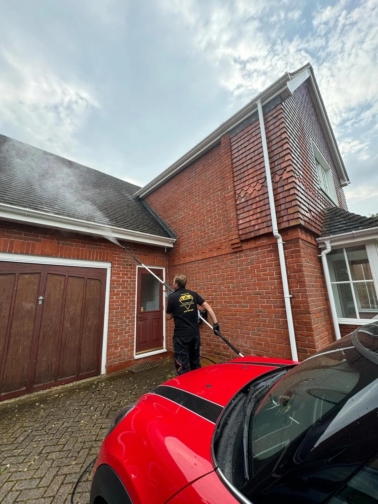Diamond Gutters UK employee using pressure washer from the ground to clean above the garage