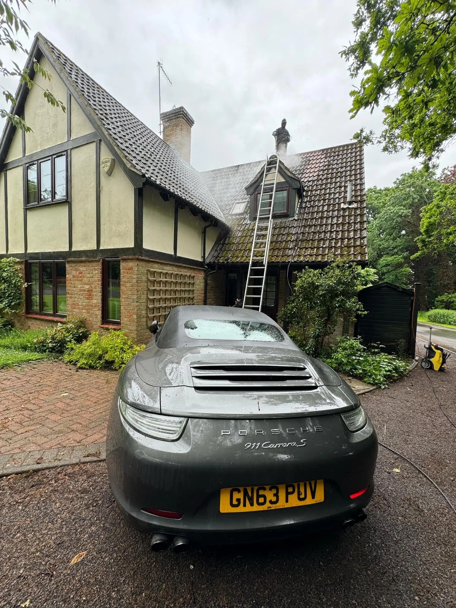 Diamond Gutters UK pressure washing the roof of a house in front of a Porsche 911